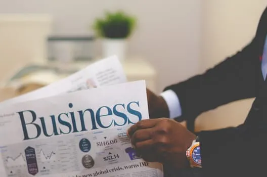 「Business」の見出しの新聞を読む人