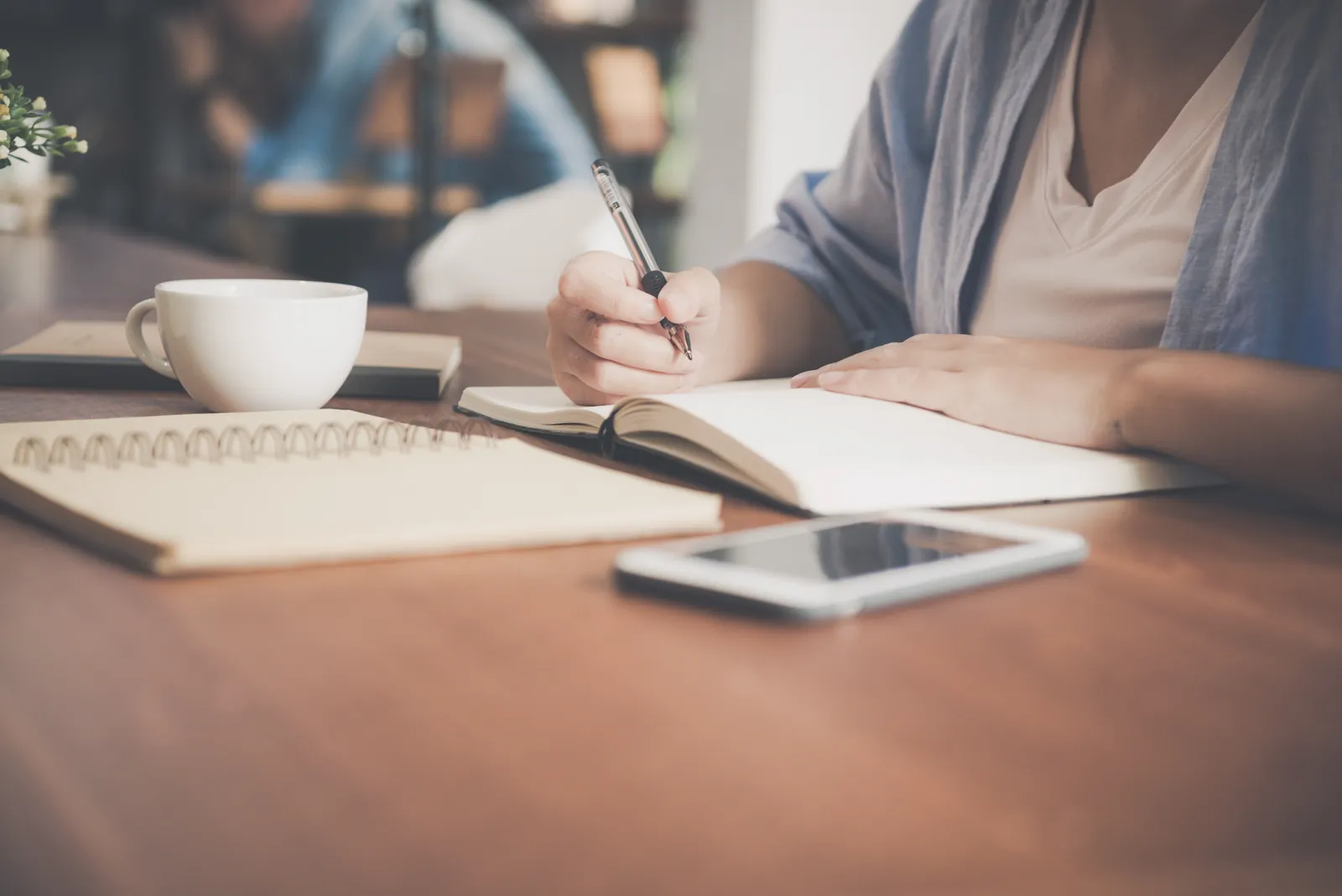 ノートにペンで書き込む人と、コーヒーカップ