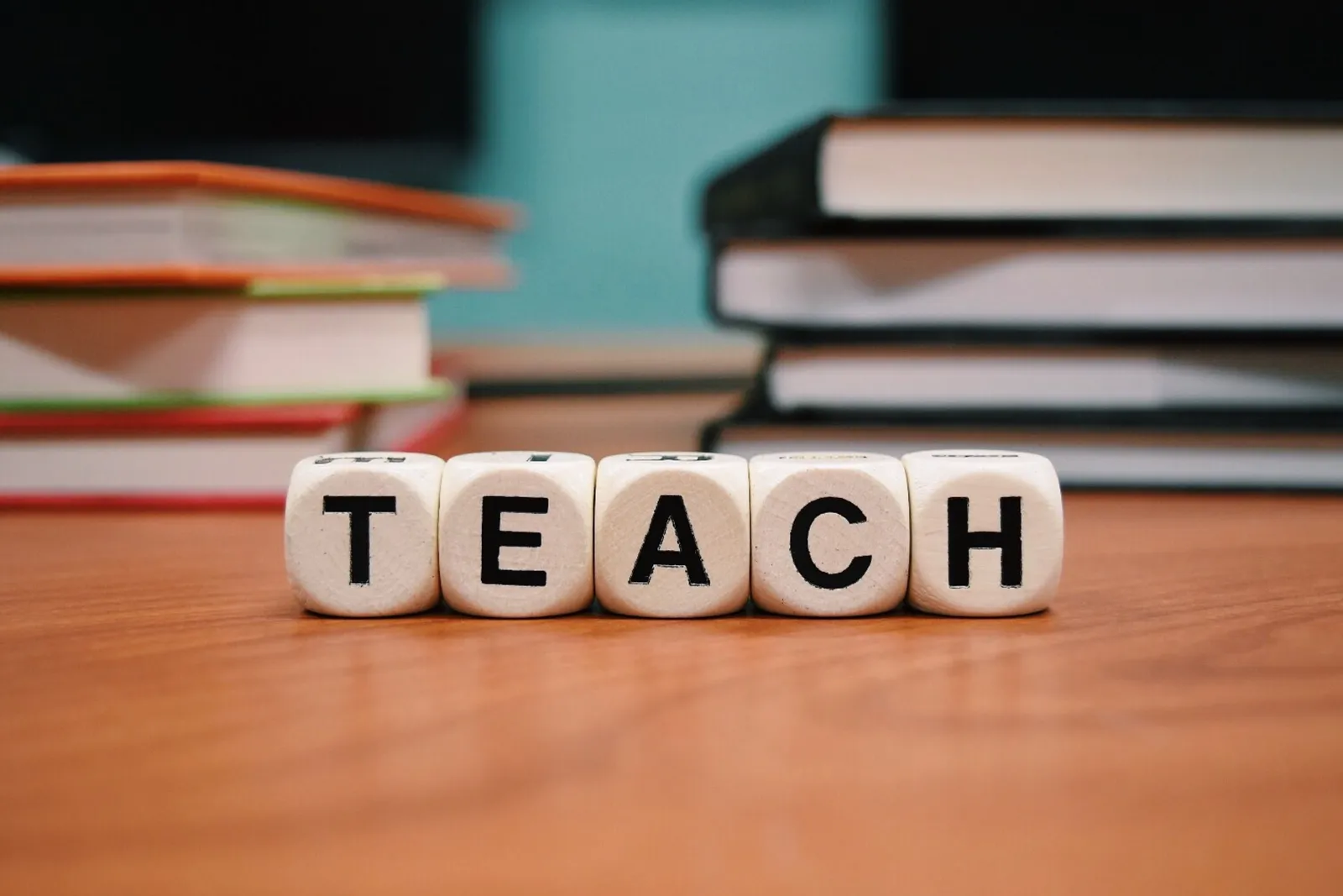 「TEACH」と並べられた文字ブロックと本