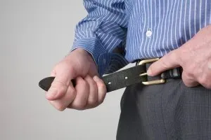 close-up image of a man in business clothes fastening his belt