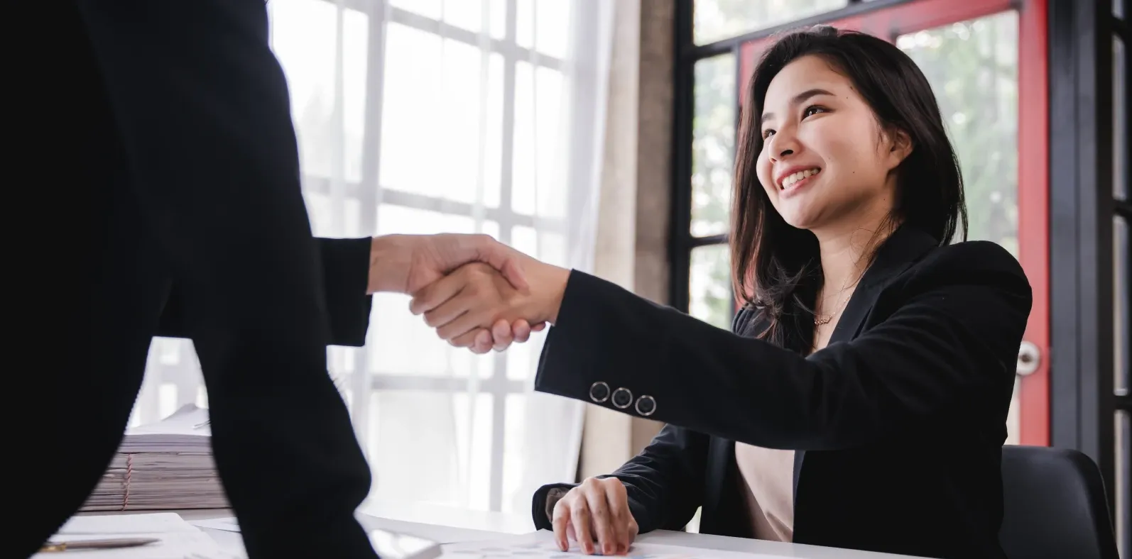 A candidate shaking hands with an interviewer across a desk