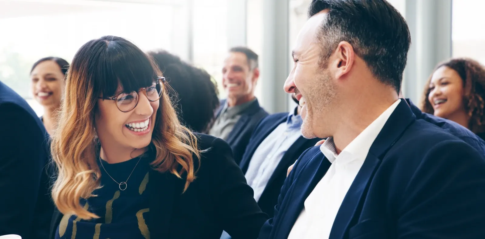 Two people laughing together in conversation at a busy event