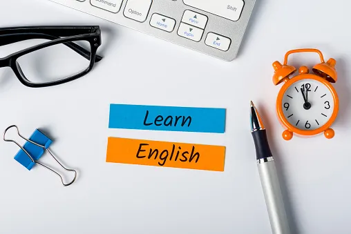 「Learn English」と書かれたラベルと、目覚まし時計、眼鏡、ペンが置かれた机