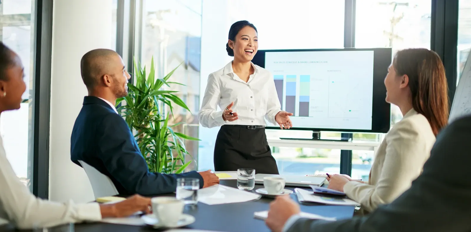 A presenter addressing colleagues beside a screen in a meeting room