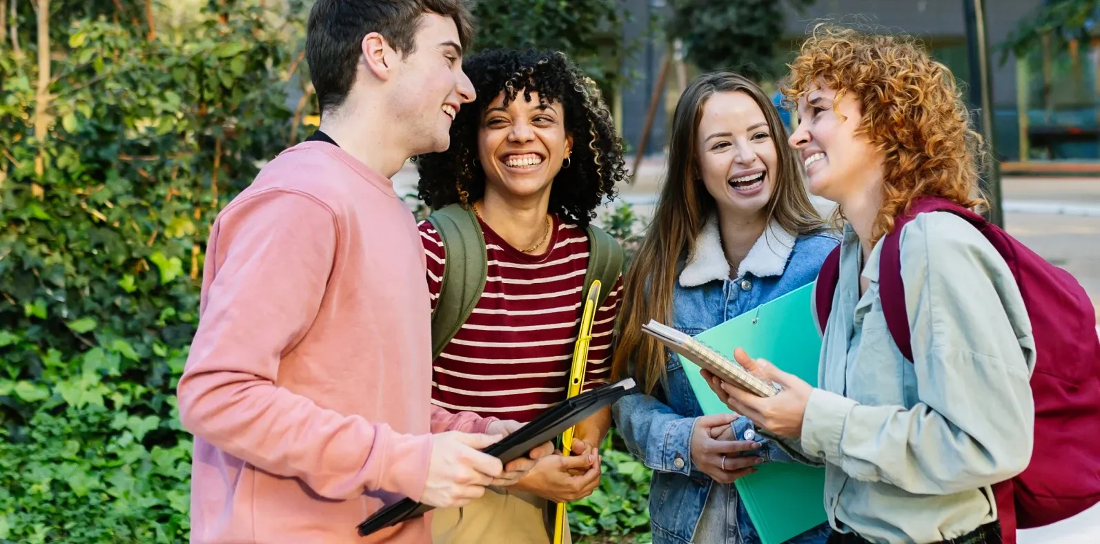 Four students talking and laughing together outside on campus