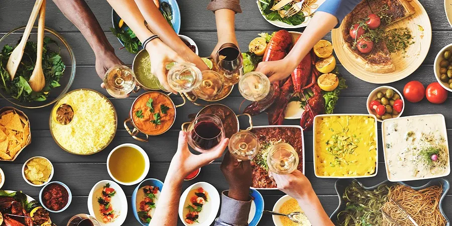 料理が並ぶテーブルでグラスを合わせる人たち