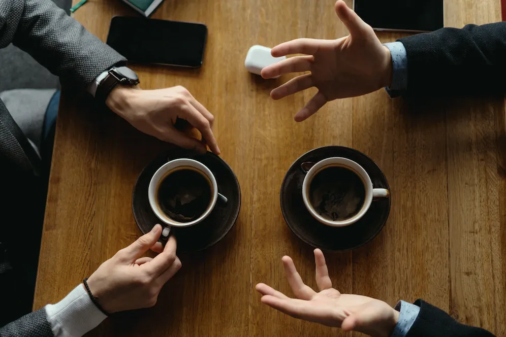 コーヒーカップを前に、身ぶりを交えて話す人たちの手