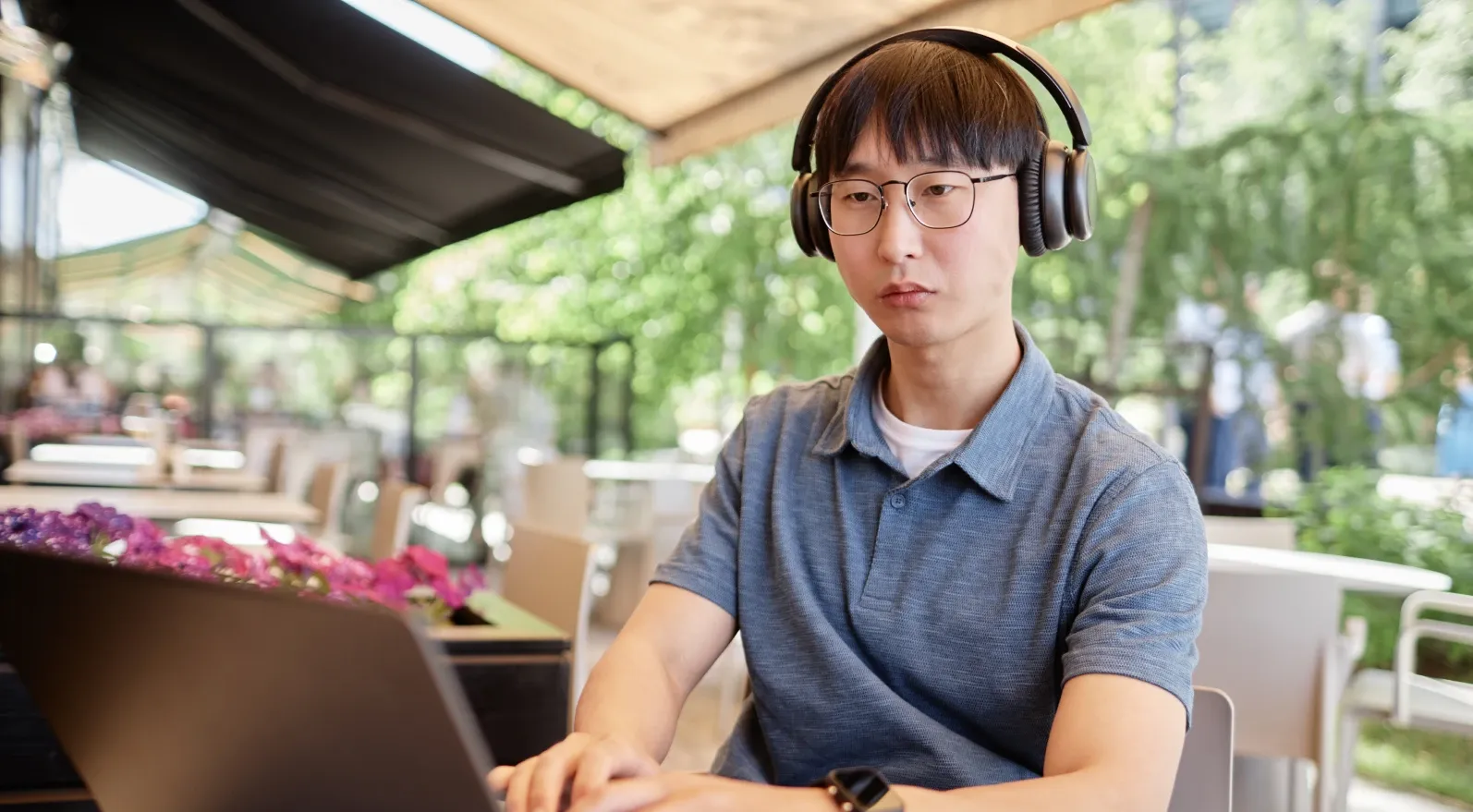 A student working at a laptop in headphones at an outdoor table