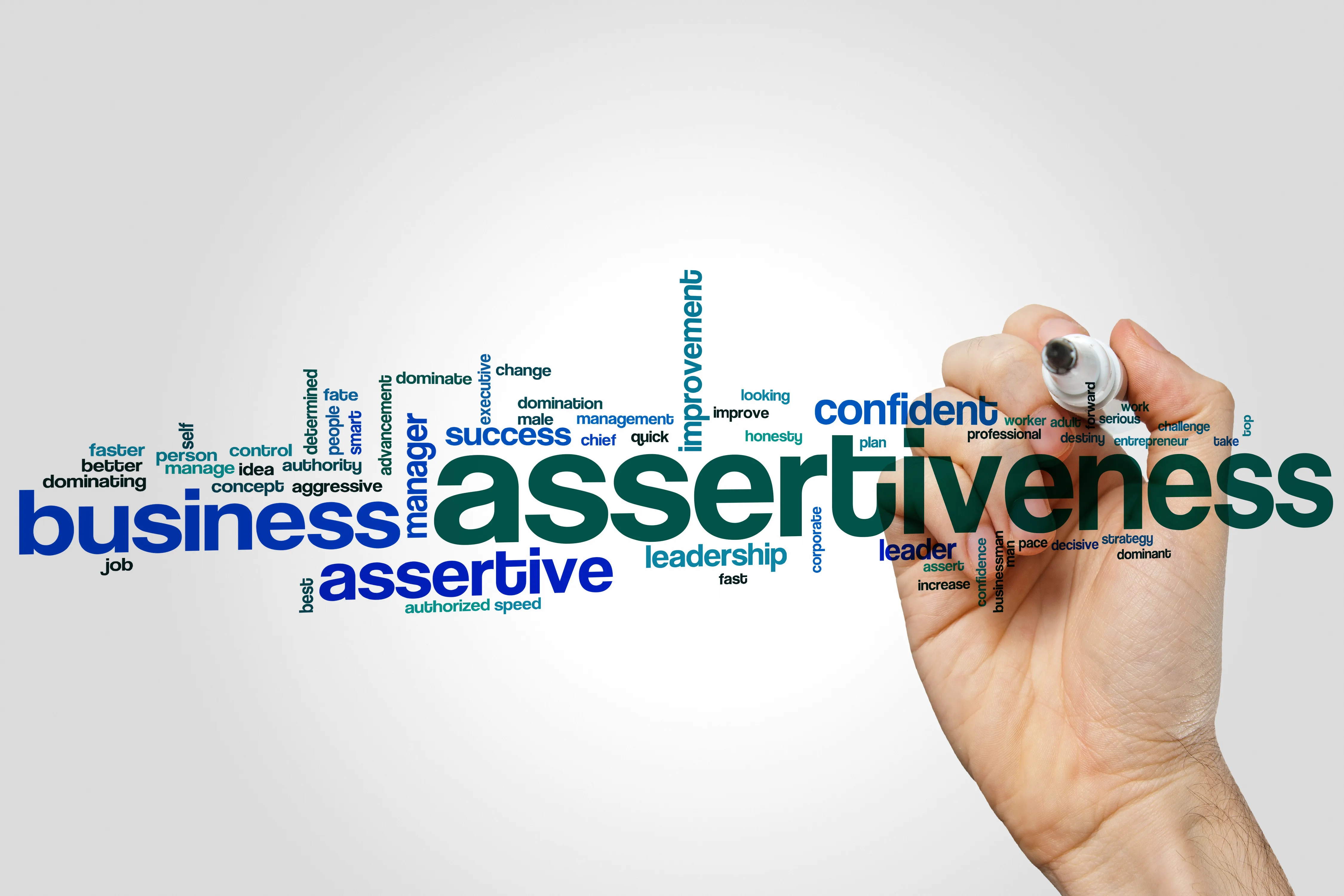 「assertiveness」を中心に関連する英単語が並ぶワードクラウドと、ペンを持つ手